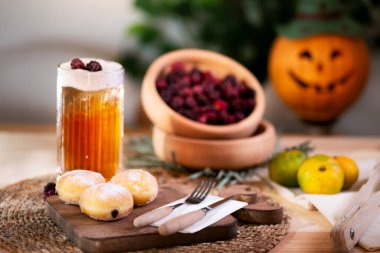 Kesme tahtasında çatal bıçaklı çikolatalı kurabiye, köpüklü elma suyu, kırmızı böğürtlen, mandalina ve arka planda bir Jack O 'Lantern ile servis edilir..