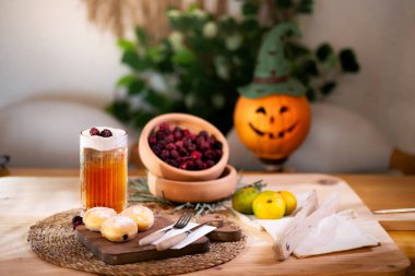 Kesme tahtasında çatal bıçaklı çikolatalı kurabiye, köpüklü elma suyu, kırmızı böğürtlen, mandalina ve arka planda bir Jack O 'Lantern ile servis edilir..