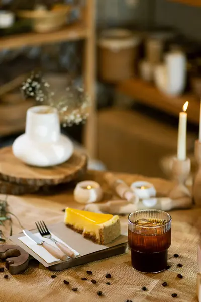 一片桔子芝士蛋糕坐在一块铺在桌布上的木板上 背景中有木制的餐具和闪亮的蜡烛 背景中散发出温暖的氛围 — 图库照片