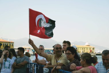 İzmir 'in Kordon bölgesinde düzenlenen Türk Zafer Günü kutlamaları sırasında, gururlu bir vatandaşın Atatrk' ın portresiyle süslenmiş Türk bayrağını salladığı görülüyor. Arka planda, ikonik Pasaport İskelesi görünür..