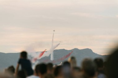 İzmir, Türkiye, 9 Eylül 2023, İzmir 'in Kurtuluş Günü' nde, tanınmış Türk Yıldızları uçakları nefes kesici hava manevralarıyla gökyüzünü boyuyor. Arkalarında kırmızı ve beyaz duman izleri bırakarak aşağıdaki dağınık kalabalığın korkusunu yakalıyorlar.