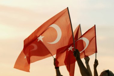 İzmir, Türkiye, Eylül, 9, 2023, gün batımında, dört birey birleşerek, canlı bir günbatımı gökyüzünün zemininde Türk bayrağını sallayarak, Kurtuluş Günü kutlamalarında birlik ve gururu sembolize ediyor..
