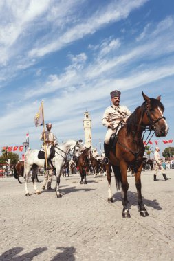 İzmir, Türkiye, Eylül, 9, 2023, Süvariler şehrin özgürlüğünü simgeleyen ikonik İzmir Saat Kulesi önünde binicilik becerilerini gururla sergiliyorlar. Günün tarihsel önemini kutlamak için poz veriyorlar.