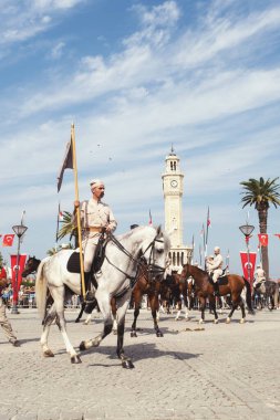 İzmir, Türkiye, Eylül, 9, 2023, Süvariler şehrin özgürlüğünü simgeleyen ikonik İzmir Saat Kulesi önünde binicilik becerilerini gururla sergiliyorlar. Günün tarihsel önemini kutlamak için poz veriyorlar.