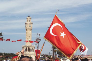 İzmir, Türkiye, 9 Eylül 2023: İzmir 'in ünlü Saat Kulesi' nin arkaplanda zarif bir şekilde durduğu bir Türk bayrağını sallayan canlı bir fotoğraf