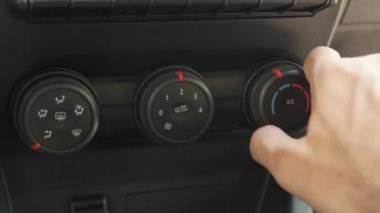 Bir arabanın klima düğmesine basan, sistemi çalıştıran ve vantilatörü çalıştıran, aracın klima kontrolünün işlevselliğini vurgulayan bir yakın çekim videosu.