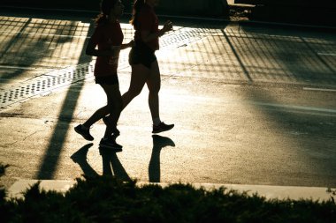 İzmir, Türkiye, 10 Eylül 2023: Koşucular İzmir Maratonu sırasında asfalt üzerindeki parlak güneş ışığına karşı siluet haline geldiler