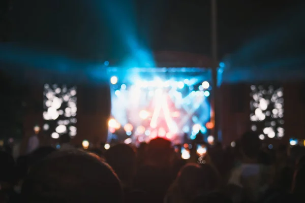 Photo capturing a lively outdoor concert at night, with people enjoying themselves, phones in hand, under the blurry glow of stage lights