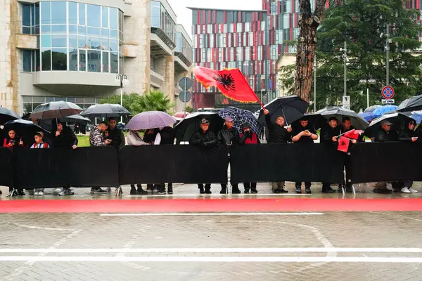 Tiran, Arnavutluk - 28 Kasım 2023: Yağmurlu bir Bağımsızlık Günü 'nde Arnavut bayrakları ve şemsiyeli vatandaşlar, ulusun şehitleri Bulvarı' ndaki geçit törenini yol kenarından izliyor.