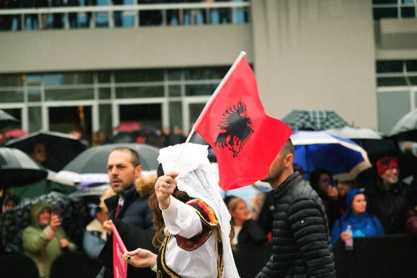 ティラナ アルバニア 11月 2023 マザーテレサ宮殿の近くの国家殉教者のアベニューでは 伝統的なドレスの女性は豪雨の独立記念日にアルバニアの旗と一緒に歩きます 背中に傘や旗を持っている見物客と — ストック写真