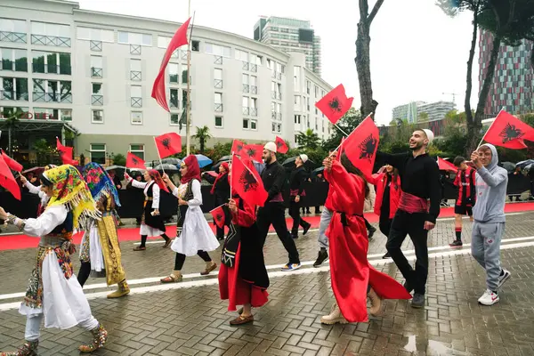 阿尔巴尼亚地拉那 2023年11月28日 在阿尔巴尼亚烈士大街上 学生和身着传统服饰的人们在一个下雨天拿着阿尔巴尼亚国旗 观众拿着雨伞和国旗 热情洋溢地走在一起 — 图库照片