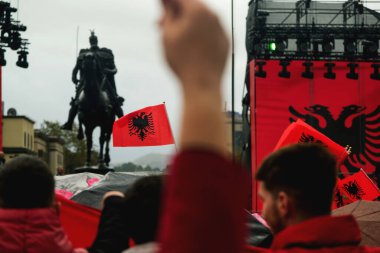 Tiran, Arnavutluk - 28 Kasım 2023: Skanderbeg Meydanı 'nda yağmurlu bir Bağımsızlık Günü' nde, iki Arnavut bayraklarıyla süslenmiş Skanderbeg heykelinin yakınındaki sahneyi ve Arnavut bayrağını taşıyan kalabalığı bir fotoğraf çekiyor.