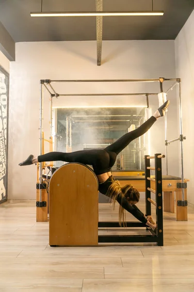 Photo of a young woman doing core exercises on a Reformer Pilates machine in a gym, focusing on her core strength