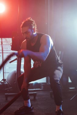 Bir atlet salıncak iplerini mavi ve kırmızı ışıkların altında sallıyor. Arka planda, sisli bir ortam, yoğunluğu arttırıyor.