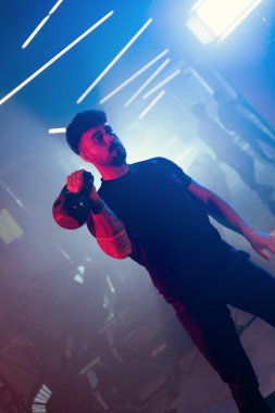 Bir adam spor salonunda kettlebell kapma gösterisi yapıyor. Sanatsal mavi ve kırmızı ışıklı ve ince sisli bir atmosferi var.