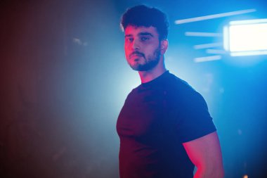 Bir erkek sporcunun portresi. Mavi ve kırmızı ışıklarla aydınlatılmış, sisli arka ışıklandırmalı bir spor salonu.