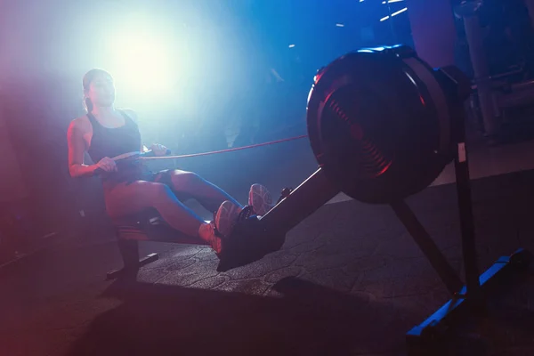 Спортзале Женщина Тренируется Гребной Машине Окружённая Мистической Смесью Синих Красных — стоковое фото