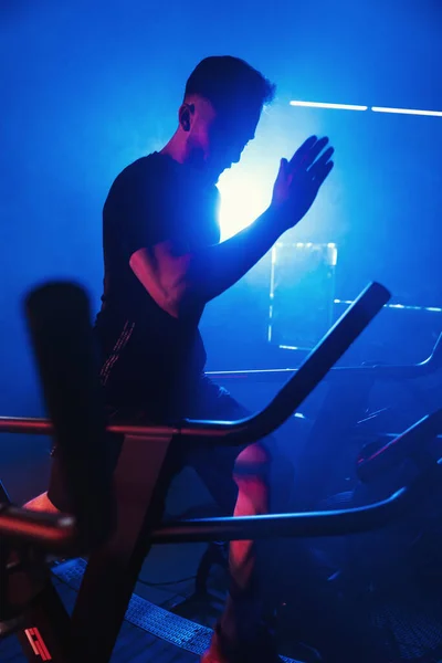 Male athlete running on a treadmill, illuminated by vivid blue and red lights creating a moody, atmospheric gym setting