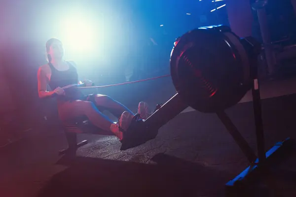 체육관에서 여성은 파란색과 빨간색 조명과 힌트의 신비한 혼합으로 둘러싸인 기계를 스톡 사진