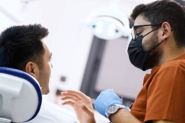 Hastasını muayene ederken yoğun konsantrasyonda olan bir dişçi, sağIıklı bir gülümseme sağlayan bir hassasiyetle uzman bakımı sağlar.