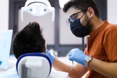 Hastasını muayene ederken yoğun konsantrasyonda olan bir dişçi, sağIıklı bir gülümseme sağlayan bir hassasiyetle uzman bakımı sağlar.