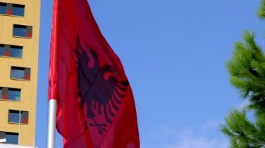 Açık havada ağır çekimde rüzgarda dalgalanan Arnavut bayrağını yakalayan fotoğraf, canlı kırmızı ve siyah renklerini vurguluyor