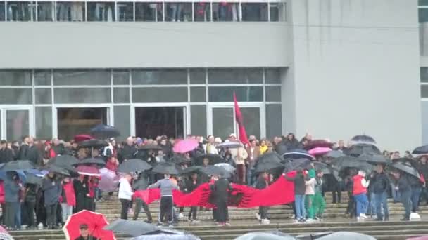 ティラナ アルバニア 11月 2023 雨の独立記念日に アルバニアの旗と傘を持つ市民は 国の大通りの殉教者の通りに道端からパレードを見ます — ストック動画