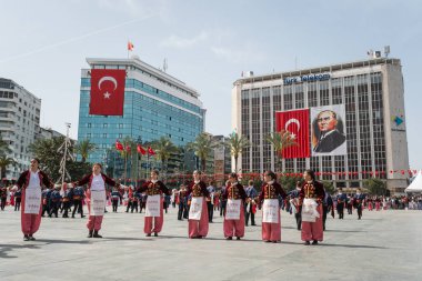 İzmir, Türkiye - 23 Nisan 2024: Geleneksel Türk kıyafetleri içindeki öğrenciler, Atatürk 'ün portresi ve Türk bayrağının arkaplanıyla Ulusal Egemenlik ve Çocuk Günü kutlamalarında kültür dansı yaptılar