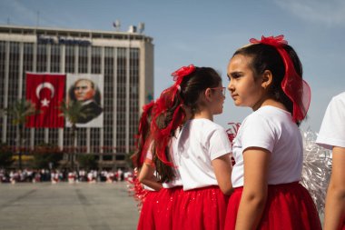 İzmir, Türkiye - 23 Nisan 2024: Kırmızı ve beyaz elbiseli kızlar, Cumhuriyet Meydanı 'nda düzenlenen Ulusal Egemenlik ve Çocuk Günü kutlamalarında sahne arkası Türk bayrakları ve bir Atatürk portresiyle performanslarını bekliyorlar