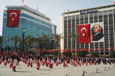 İzmir, Türkiye - 23 Nisan 2024: Geleneksel Türk kıyafetleri içindeki öğrenciler, Atatürk 'ün portresi ve Türk bayrağının arkaplanıyla Ulusal Egemenlik ve Çocuk Günü kutlamalarında kültür dansı yaptılar