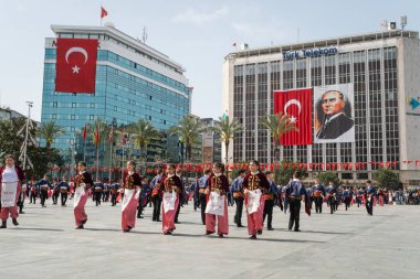 İzmir, Türkiye - 23 Nisan 2024: Geleneksel Türk kıyafetleri içindeki öğrenciler, Atatürk 'ün portresi ve Türk bayrağının arkaplanıyla Ulusal Egemenlik ve Çocuk Günü kutlamalarında kültür dansı yaptılar