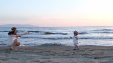 Bir yaşındaki bir çocuk gün batımında Özbek annesine doğru koşuyor. Arka planda okyanus dalgalarıyla kumda oynarlar.