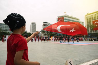 İzmir, Türkiye - 19 Mayıs 2024: Cumhuriyet Meydanı 'nda Gençlik ve Spor Günü ve Atatürk Anma Günü kutlamalarında gençlerin performansını izlerken genç bir çocuk Türk bayrağı sallıyor
