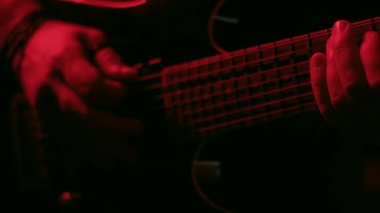 Kırmızı ışık altında ustalıkla gitar çalan bir elin yakın plan videosu ayrıntılı parmak hareketlerini ve dramatik atmosferi vurguluyor