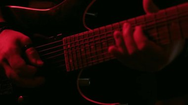 Kırmızı ışık altında ustalıkla gitar çalan bir elin yakın plan videosu ayrıntılı parmak hareketlerini ve dramatik atmosferi vurguluyor