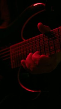Kırmızı ışık altında ustalıkla gitar çalan bir elin yakın plan videosu ayrıntılı parmak hareketlerini ve dramatik atmosferi vurguluyor