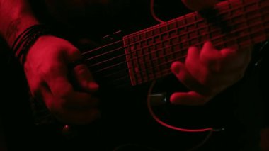 Kırmızı ışık altında ustalıkla gitar çalan bir elin yakın plan videosu ayrıntılı parmak hareketlerini ve dramatik atmosferi vurguluyor