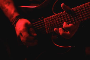 Kırmızı ışıkta ustaca gitar çalan bir elin detaylı yakın çekimi performansın yoğunluğunu ve duygusunu vurguluyor.