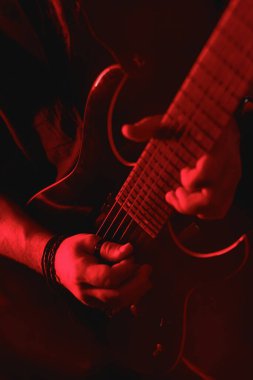 Kırmızı ışıkta ustaca gitar çalan bir elin detaylı yakın çekimi performansın yoğunluğunu ve duygusunu vurguluyor.