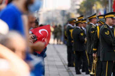 İzmir, Türkiye - 30 Ağustos 2024: Zafer Günü kutlamalarında arka planda askeri performans için hazırlanmış askerlerle birlikte bir Türk bayrağının yakın çekimi.