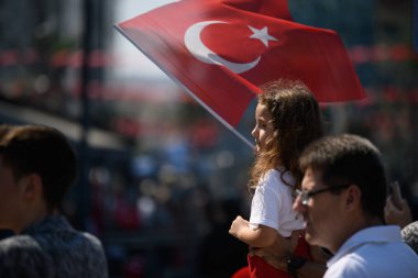 İzmir, Türkiye - 30 Ağustos 2024: Elinde Türk bayrağı olan genç bir kız, Zafer Günü 'nü merakla ve gururla izliyor ve ulusun geleceğini simgeliyor.