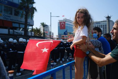 İzmir, Türkiye - 30 Ağustos 2024: Elinde Türk bayrağı olan genç bir kız, Zafer Günü 'nü merakla ve gururla izliyor ve ulusun geleceğini simgeliyor.