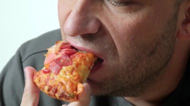 Bir adamın pizza diliminden bir ısırık alışını gösteren yakın plan bir video, pizzanın dokusunu ve yerken adamın ağzını vurguluyor.