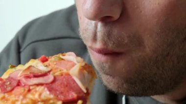 Bir adamın pizza diliminden bir ısırık alışını gösteren yakın plan bir video, pizzanın dokusunu ve yerken adamın ağzını vurguluyor.