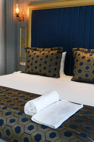 stock image Close-up of a hotel room bed with rolled white towels and geometric patterned cushions, creating a luxurious and inviting ambiance