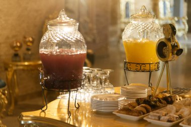 Bir çift bavulla el ele tutuşarak lüks bir otel lobisine girer. Altın dekorlar ve avizelerle süslenir. Zarafet ve stili yansıtır.