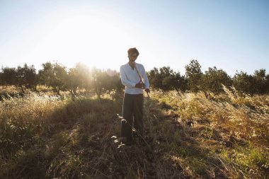 Beyaz gömlekli 40 yaşında bir adam zeytin tarlasında altın güneş ışığıyla yıkanırken ney flütü çalıyor. Doğa ve barışçıl bir atmosfer ile çevrili