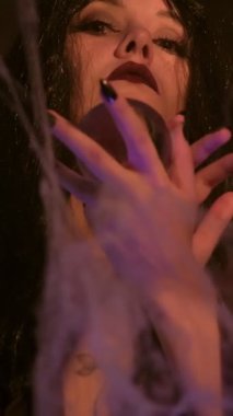 Bir cadı sanki büyü yapıyormuş gibi ellerini kristal kürenin etrafında gezdiriyor. Yakın plan video, elleri örümcek ağlarıyla çevrili uzun siyah tırnaklarla mistik bir titreşim yaratıyor.
