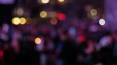 Konserden keyif alan bir kalabalığın yavaş çekim, arka planda renkli ışıkları aydınlatan yumuşak, bulanık bir bokeh efektiyle, canlı ambiyansı yakalıyor.
