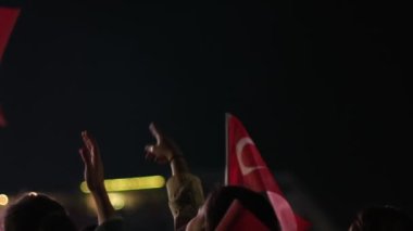 Karanlık bir gökyüzüne karşı Türk bayrağını ağır çekimde tutan ve sallayan bir kişi, ulusal gurur ve kutlamaları vurguluyor